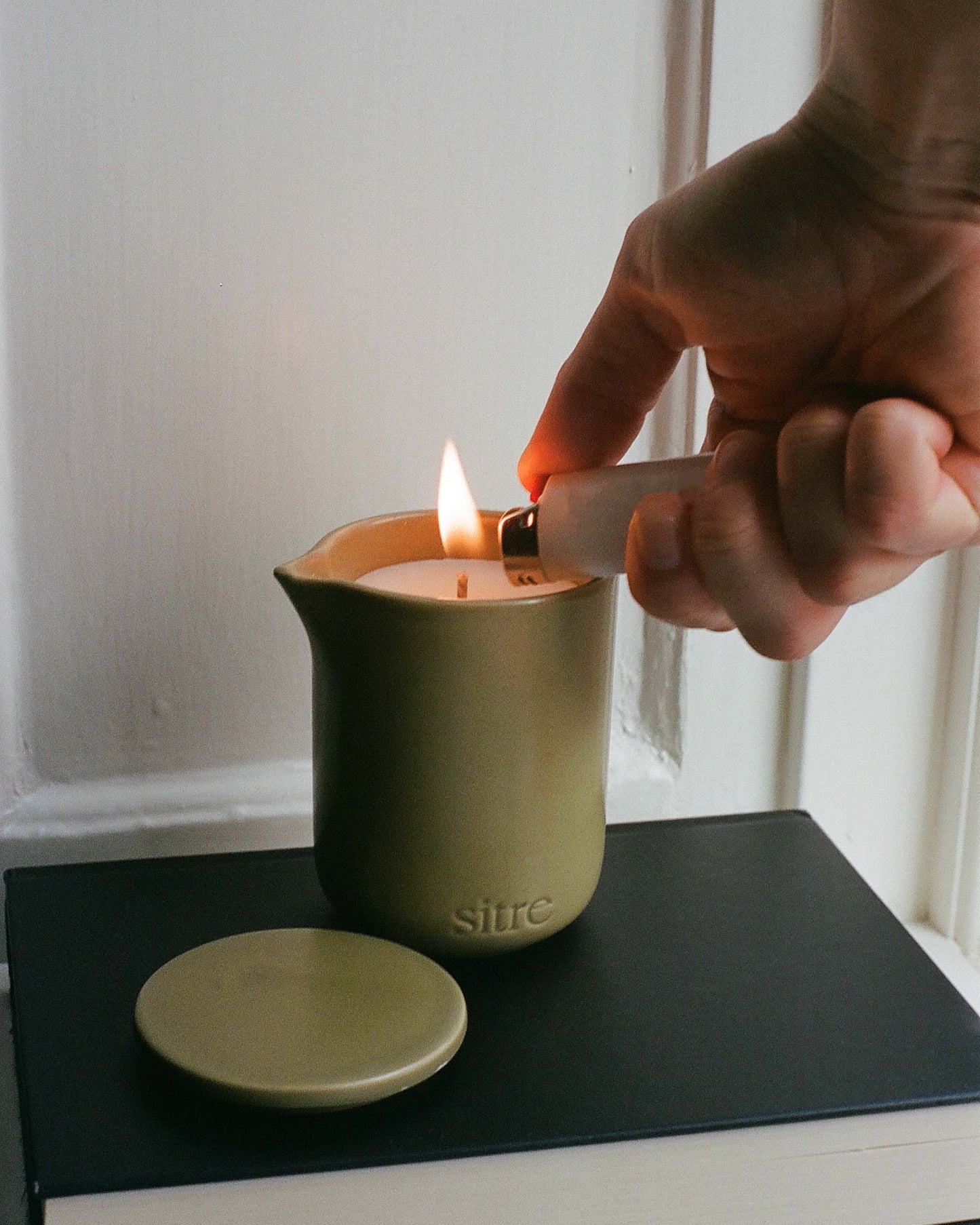 Hand lighting a massage candle with a match on a black surface.