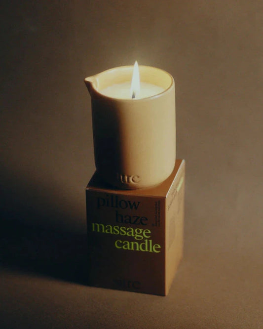 Lit candle on a box labeled 'pillow haze massage candle' against a dark background