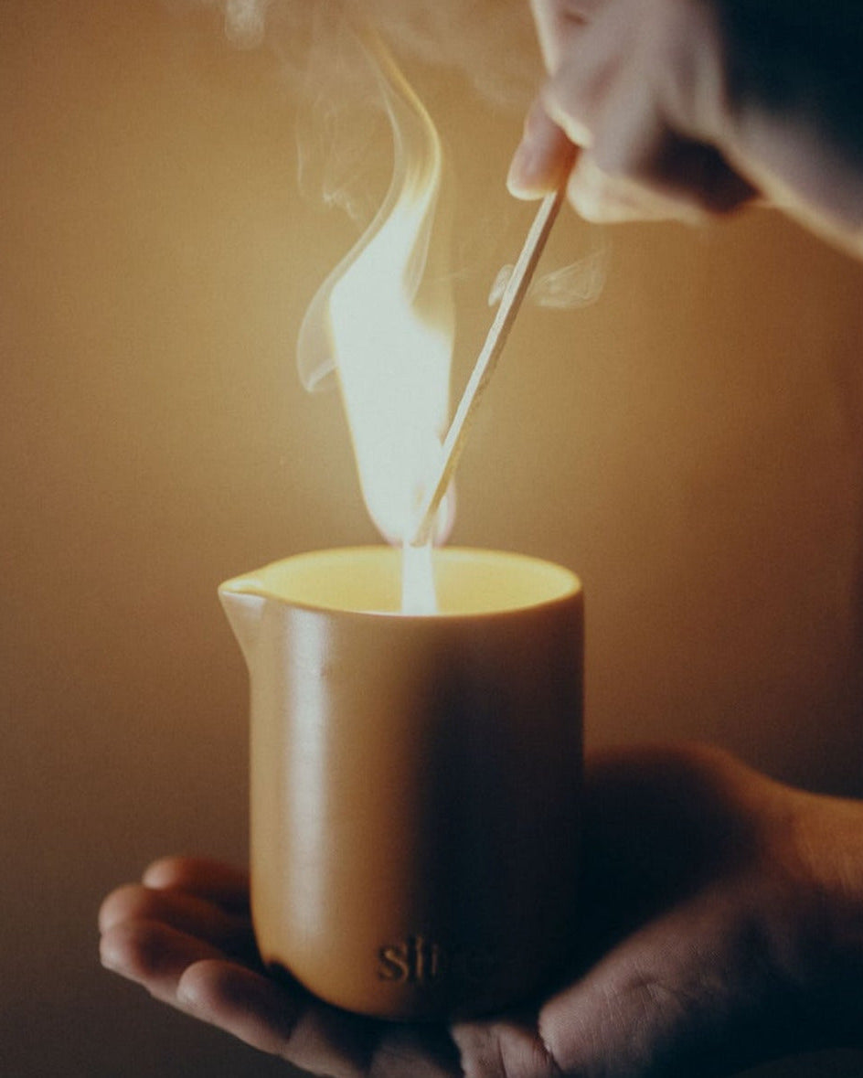 Person lighting a massage candle with a match, held in a warm-toned setting.