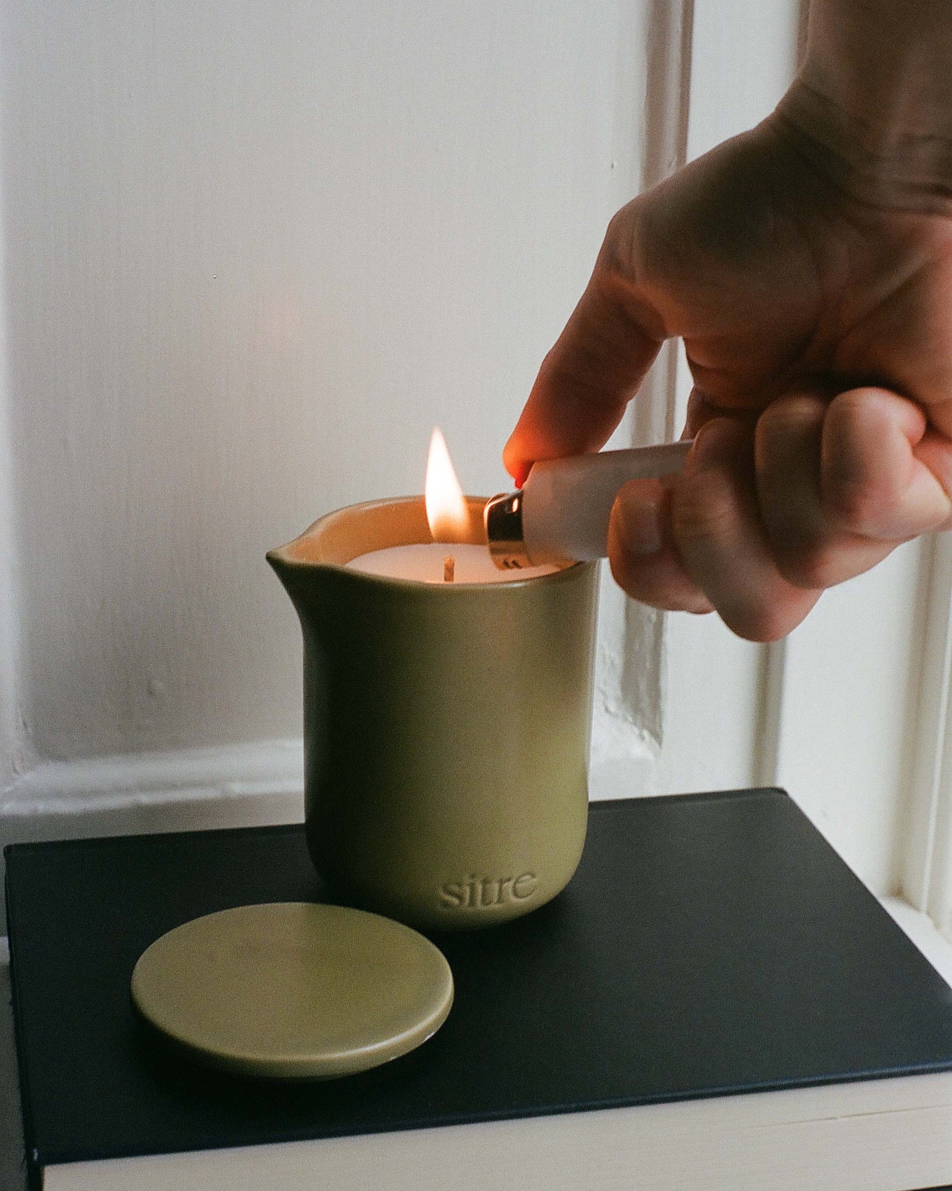 Hand lighting a massage  candle with a match on a black surface.